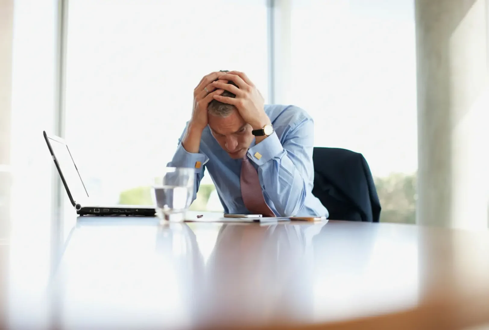 A stressed businessman sitting at an office desk with his head in his hands, illustrating the overwhelming feelings associated with depression vs anxiety in the workplace.