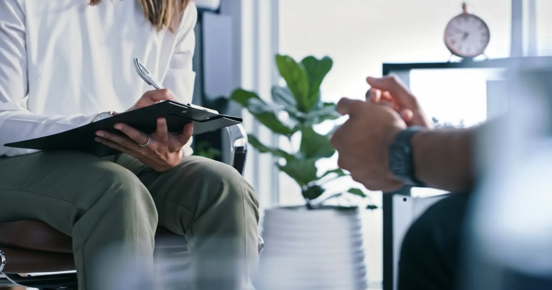A psychiatrist taking detailed clinical notes on a clipboard during a private mental health assessment with a patient.