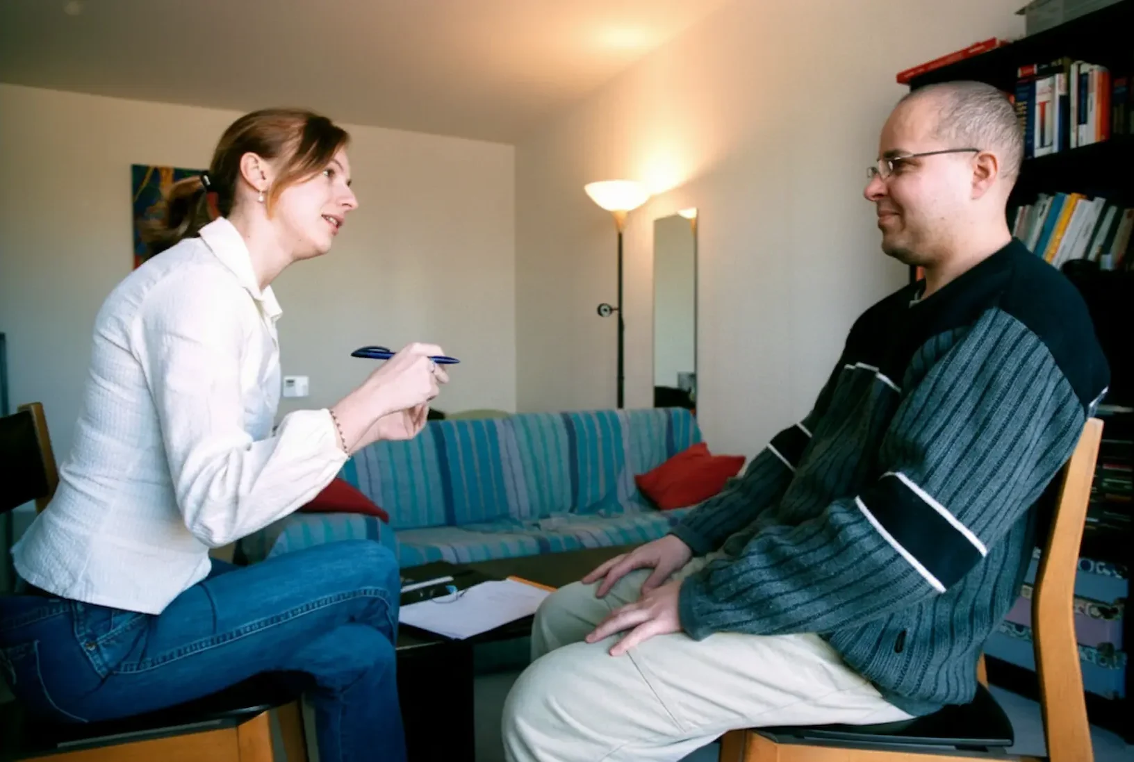 A female clinician actively engaging in a mental health evaluation with a male patient in a comfortable, residential-style office setting.