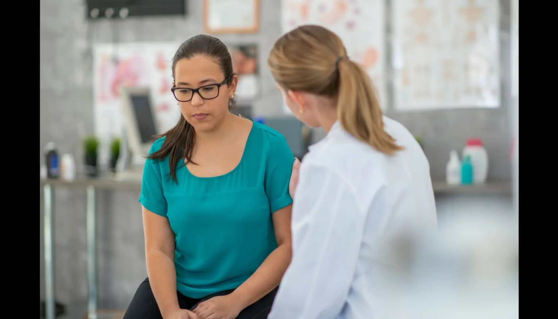 A healthcare professional in a white coat offering support to a young woman during a psychiatric appointment in a medical office.