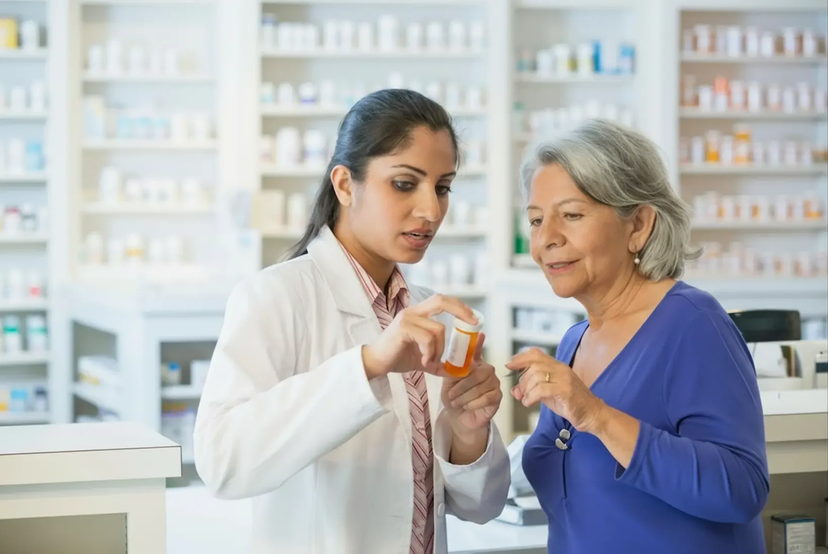 A female pharmacist in a white lab coat explaining prescription details to a senior woman, demonstrating professional psychiatric medication management and medication safety.
