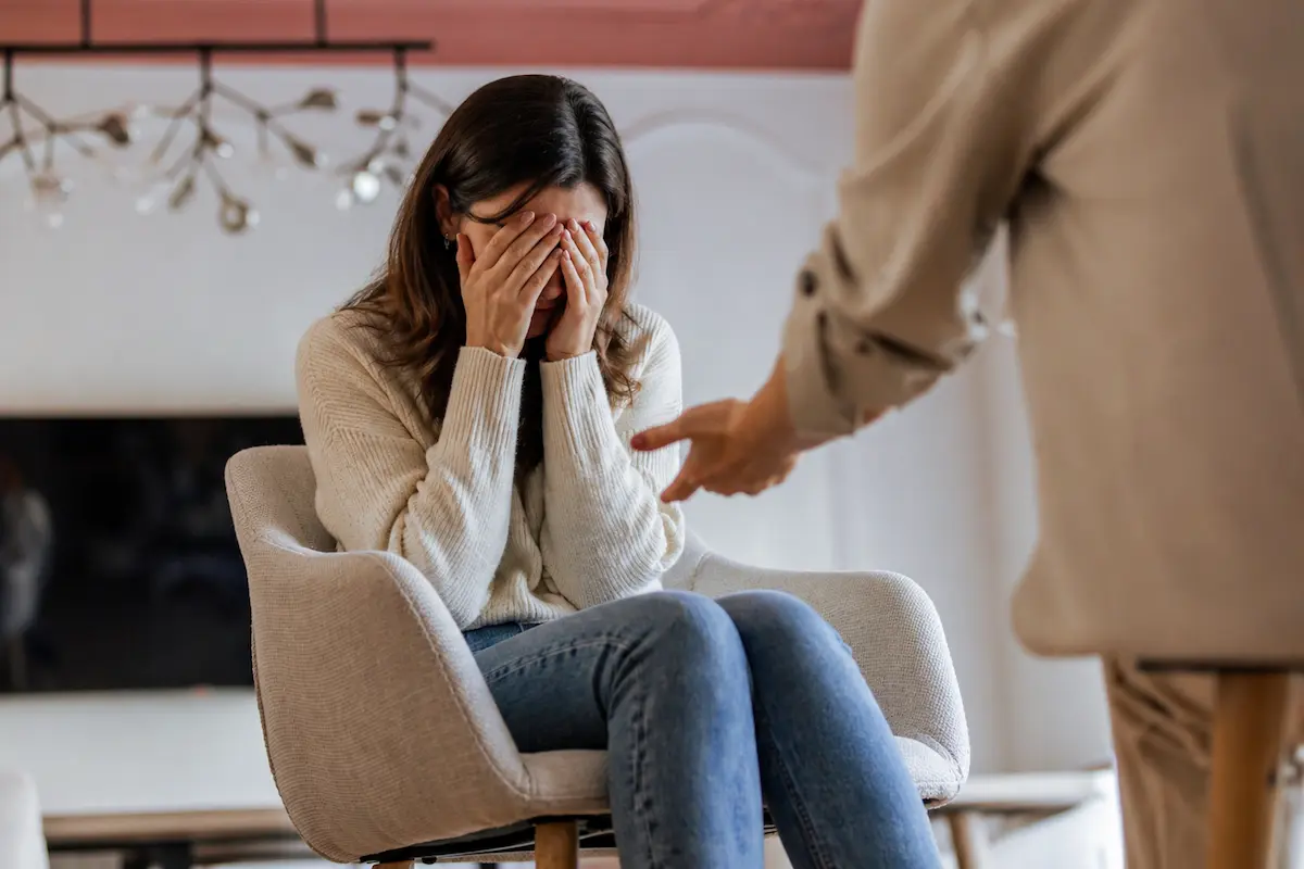Woman covering her face in distress during a therapy session for mood disorder, receiving support from a mental health professional.