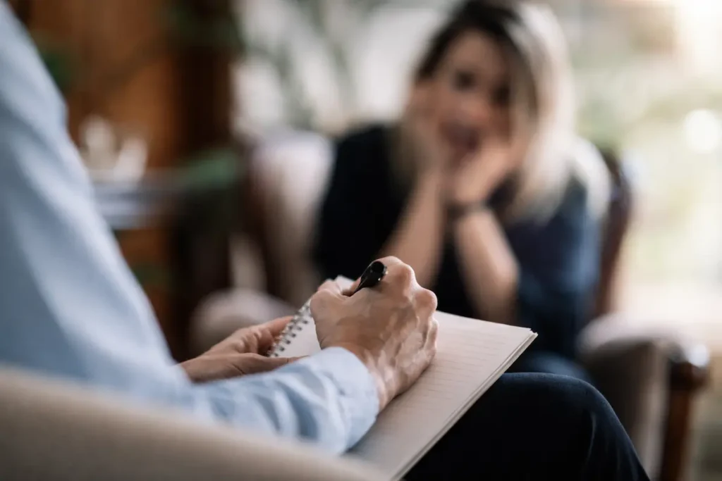 Therapist writing notes during psychiatric treatment session with patient in counseling setting