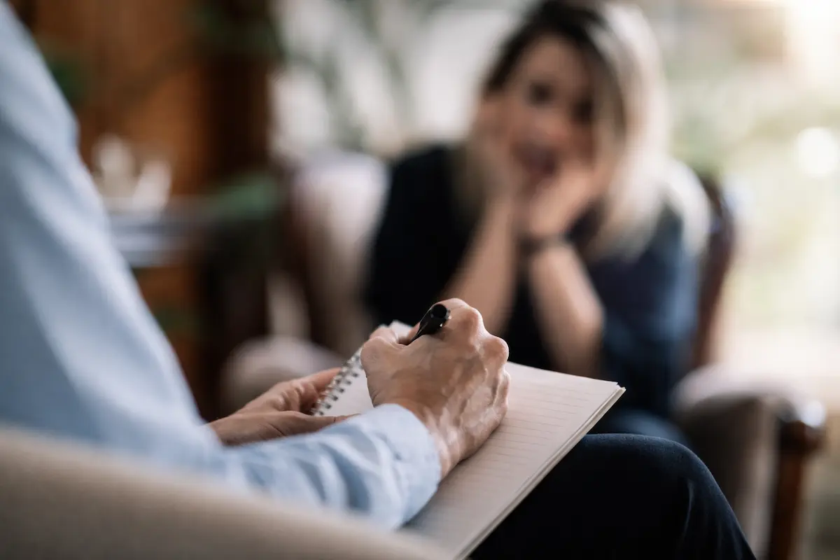 Therapist writing notes during psychiatric treatment session with patient in counseling setting