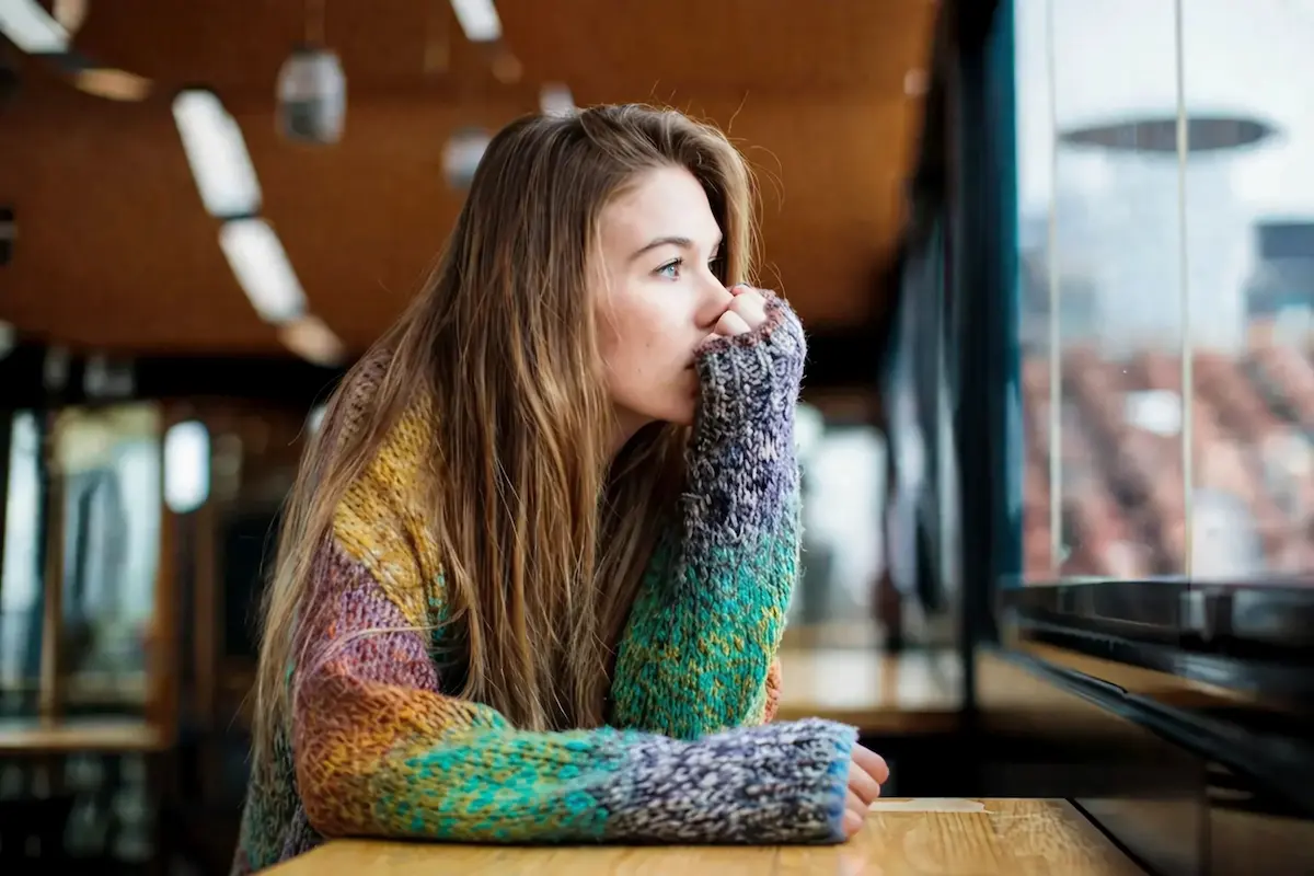 Woman sitting alone by a window looking thoughtful, representing anxiety and depression