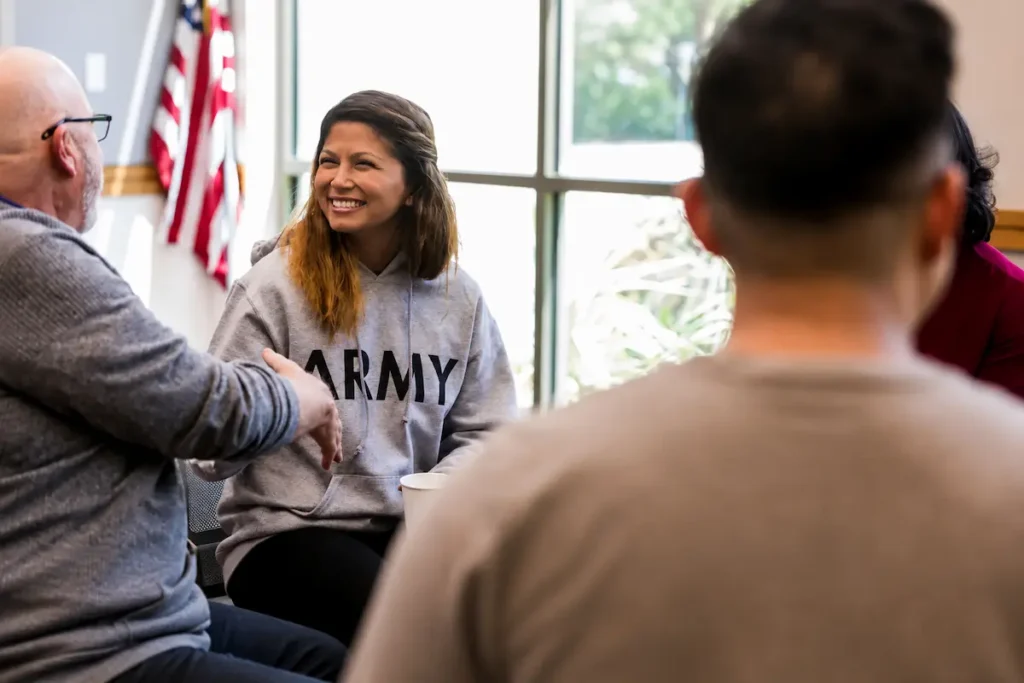 Military veteran wearing an ARMY hoodie smiling during a PTSD support group session, illustrating common signs of PTSD and the importance of peer support and mental health treatment.